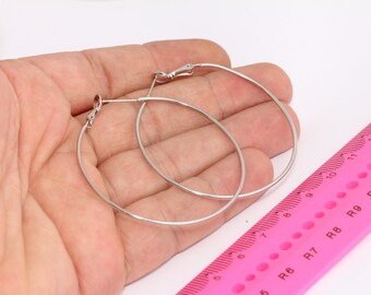 May include: A pair of silver hoop earrings, measuring approximately 9 cm in diameter, are held in a hand against a pink ruler.