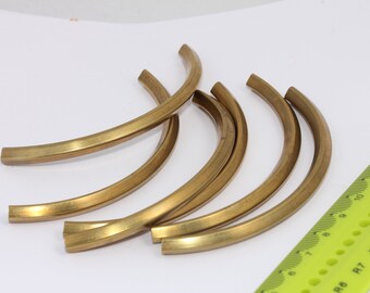 May include: Six gold-colored metal strips, each bent into a semi-circular shape. The strips are arranged in a pile, with the ruler visible in the background.