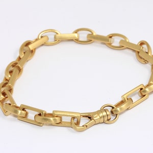 May include: A gold chain bracelet with a clasp closure. The chain is made of interlocking oval and rectangular links.
