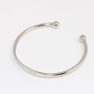 Może przedstawiać: Srebrna bransoletka typu bangle z zaokrąglonymi końcami. Bransoletka jest prosta i minimalistyczna.