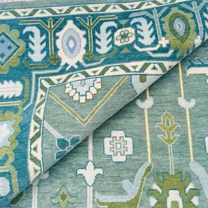 May include: A teal blue rug with a geometric pattern in shades of green, white, and blue. The rug has a folded edge, revealing the underside.