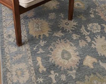 May include: A rectangular area rug featuring a deep blue background with a repeating pattern of stylised floral and botanical motifs in muted shades of beige, sage green, and light blue, finished with a decorative border along the edges.