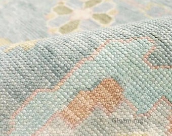 May include: Close-up of a light blue, pink, and green patterned rug. The rug has a woven texture and a subtle sheen. The text "Gleam rug" is visible in the top left corner of the image.