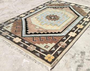 May include: A vintage rug with a geometric pattern in shades of brown, blue, and beige. The rug has a fringe border and features the text "Gleam rugs" in the bottom right corner.