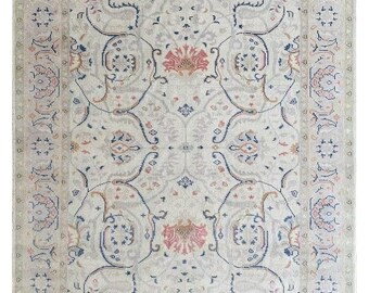May include: A beige rug with a floral pattern in shades of pink, blue, and brown. The rug has a fringe border.