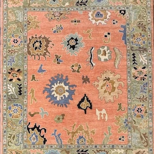 May include: A rectangular area rug with a salmon-colored center and a green border. The rug features a repeating floral pattern in shades of blue, brown, and cream. The rug has a fringe on the short ends.