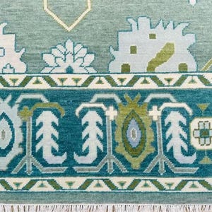 May include: A teal blue rug with a white and green geometric pattern. The rug has a fringe border.