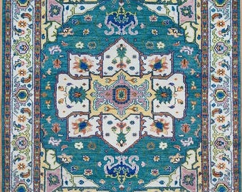May include: A teal blue rug with a white, yellow, and pink geometric pattern. The rug has a traditional design with intricate details.
