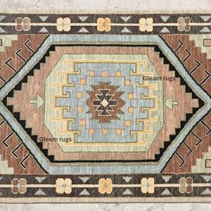 May include: A beige rug with a brown, blue, and beige geometric pattern. The rug has a fringe border and the text "Gleam rugs" is visible twice in the image.