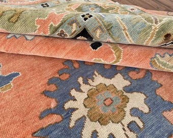 May include: A close-up of a rug with a floral pattern. The rug is made of wool and has a soft, plush texture. The colours of the rug are peach, blue, and beige.