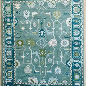 May include: A teal blue rug with a geometric pattern in shades of green, white, and blue. The rug has a border with a repeating design.