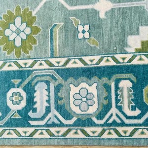 May include: A teal blue rug with a white and green floral pattern. The rug has a border with a repeating pattern of white, green, and teal blue.