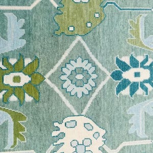 May include: A close-up of a blue rug with a repeating pattern of green, blue, and white floral designs. The rug has a soft, textured surface.