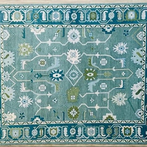May include: A teal blue rug with a geometric pattern in shades of green, white, and blue. The rug has a border with a repeating design.