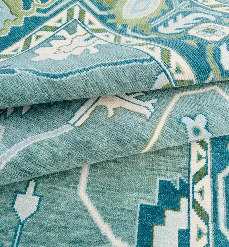 May include: A teal blue rug with a white and green geometric pattern. The rug is folded in half, showing the intricate details of the design.