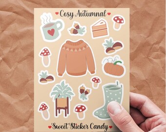 Op de afbeelding: Een vel met stickers met een herfstthema. De stickers bevatten een mok met warme chocolademelk, een trui, een pompoen, een plant in een pot, regenlaarzen, paddenstoelen, eikels en een stuk taart. De tekst "Cosy Autumnal" en "Sweet Sticker Candy" staat op het vel gedrukt.