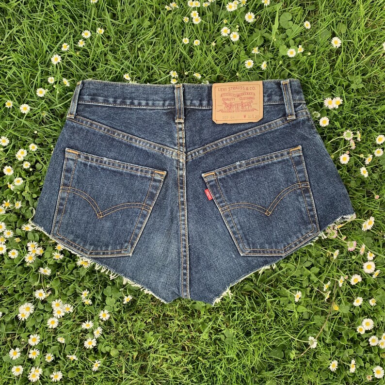 May include: Dark blue denim shorts with frayed edges. The shorts have a back pocket with a red Levi's tab and a brown leather patch with the Levi's logo and text that reads "Levi Strauss & Co. San Francisco, Calif. Original Quality Clothing. WPL 423."
