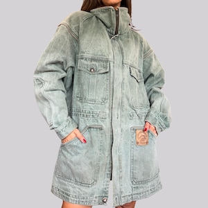 Può includere: Una giacca in denim verde salvia sbiadito con collo alto, maniche lunghe e chiusura frontale con zip. La giacca presenta due tasche sul petto con patta, due ampie tasche applicate sul fondo e una toppa rettangolare in pelle sul lato sinistro.