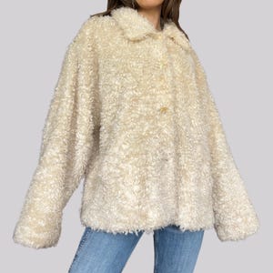 May include: A cream-coloured, fluffy coat with a button closure and a collar. The coat has a textured, curly appearance and long sleeves. The garment is a neutral colour, suitable for various outfits.