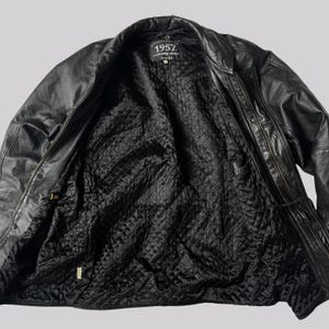 May include: Black leather jacket with a quilted black lining. The jacket has a zipper closure and a collar. The label inside the jacket reads "1957". The jacket is open, showing the interior lining.