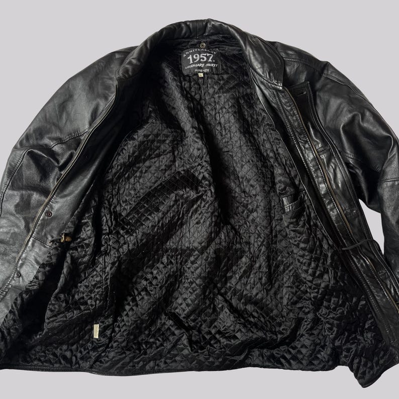 May include: Black leather jacket with a quilted black lining. The jacket has a zipper closure and a collar. The label inside the jacket reads "1957". The jacket is open, showing the interior lining.
