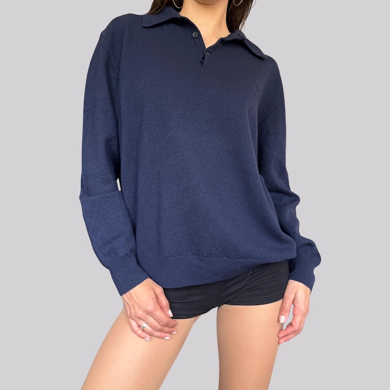 K&ouml;nnte beinhalten: Marineblaues Langarm-Poloshirt mit Kragen und zwei Kn&ouml;pfen. Das Shirt hat ein kleines Logo auf der Brust. Das Shirt ist aus einem weichen, bequemen Material gefertigt.