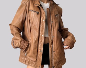Könnte beinhalten: Hellbraune Lederjacke mit klassischem Design. Die Jacke hat einen Reißverschluss, mehrere Taschen und einen Kragen. Das Leder hat ein leicht abgenutztes Aussehen, was ihm einen Vintage-Look verleiht. Die Jacke ist hellbraun.
