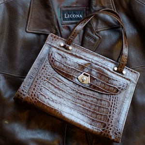 May include: A brown crocodile-embossed leather handbag with a gold-toned clasp and the word "LICONA" on the front.