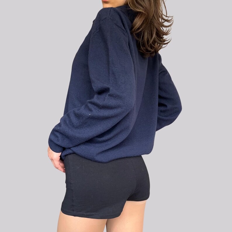K&ouml;nnte beinhalten: Ein marineblaues Sweatshirt mit langen &Auml;rmeln und schwarze Shorts. Das Sweatshirt hat einen Rundhalsausschnitt und eine lockere Passform. Die Shorts sind schwarz und scheinen aus einem dehnbaren Material zu sein. Das Outfit ist einfach und l&auml;ssig.