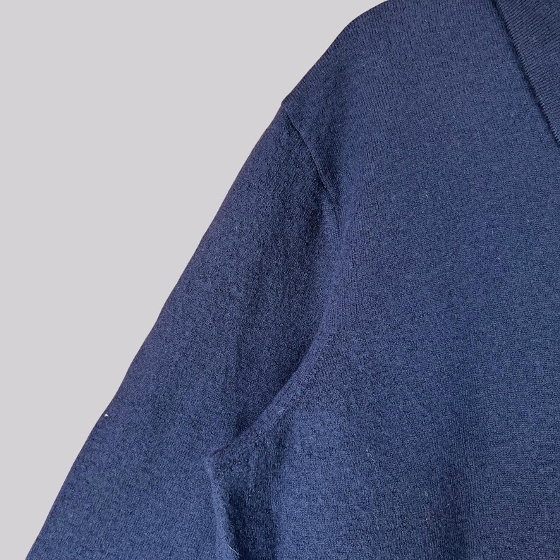 K&ouml;nnte beinhalten: Nahaufnahme eines marineblauen Pullovers. Der Stoff hat eine strukturierte Optik, und der Halsausschnitt ist sichtbar. Der Pullover scheint aus einem weichen Material zu sein, das f&uuml;r k&uuml;hlere Temperaturen geeignet ist. Das Bild ist gut beleuchtet und hebt die Details des Strickwerks hervor.