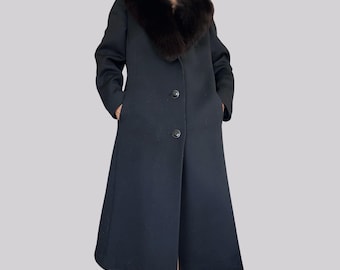 May include: A long black coat featuring a large, dark brown fur collar, long sleeves, and two visible black buttons down the front. The coat has a structured silhouette with a flared hemline and two side pockets, providing a classic, full-length look.
