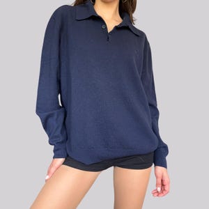 K&ouml;nnte beinhalten: Ein marineblaues Polohemd mit langen &Auml;rmeln, einem Kragen und zwei Kn&ouml;pfen. Das Hemd hat ein kleines Logo auf der Brust und ist aus weichem Strickmaterial gefertigt. Das Hemd ist ein klassischer Stil.