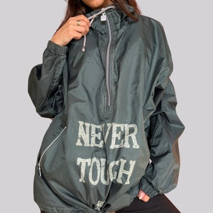 Könnte beinhalten: Eine dunkelgrüne Kapuzenjacke mit Reißverschluss und dem Aufdruck "NEVER TOUGH" auf der Vorderseite.