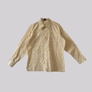 Puede incluir: Una camisa de manga larga con botones, fondo crema y estampado geométrico en blanco y negro.
