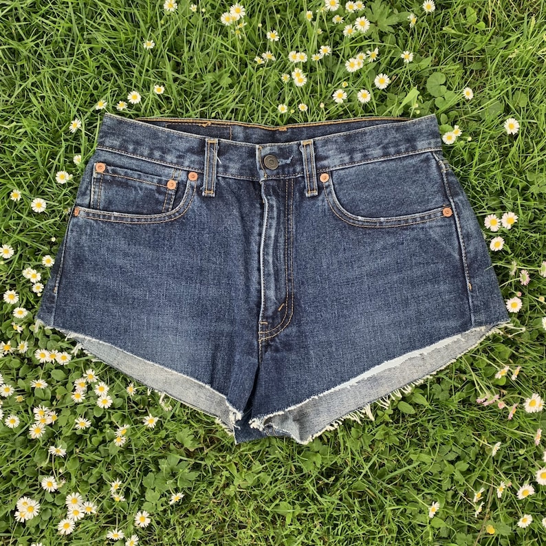 May include: Dark blue denim shorts with a frayed hem. The shorts have a high waist and are made of a thick, durable fabric.