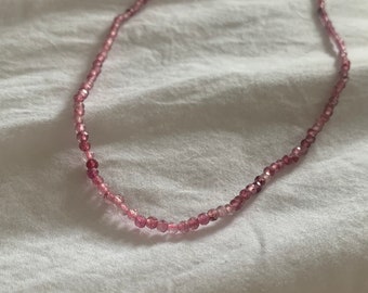 Puede incluir: Un delicado collar de cuentas de vidrio rosa y transparente con un cierre dorado.
