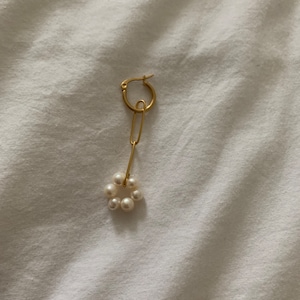May include: A gold hoop earring with a dangling chain and a circle of pearls.