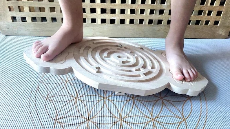 May include: A wooden balance board with a circular maze pattern on the top. A person is standing on the board with their feet on the edges.