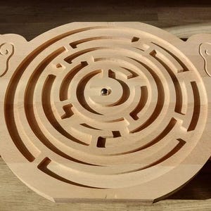 May include: A wooden maze game with a circular maze in the center and two foot-shaped pieces on either side. The maze has a small metal ball in the center.