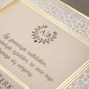 May include: A wedding invitation with a gold border and a white background. The invitation features a wreath with the initials "A.B." in the centre. The text reads "Good days we share happiness, bad days we share sorrow. We promise to share both for a lifetime."