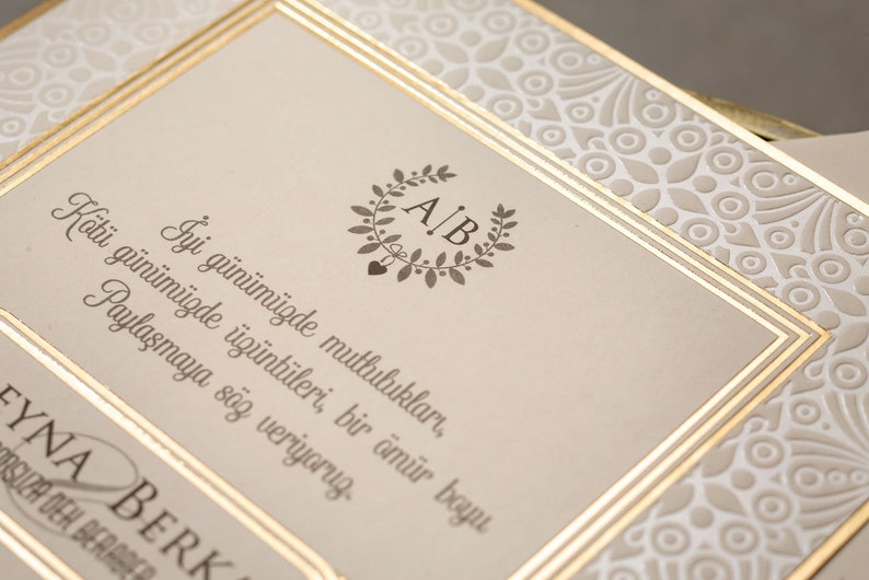 May include: A wedding invitation with a gold border and a white background. The invitation features a wreath with the initials "A.B." in the centre. The text reads "Good days we share happiness, bad days we share sorrow. We promise to share both for a lifetime."