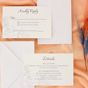 May include: Wedding invitation suite with RSVP and details cards, and white envelopes. The cards are off-white with floral line art and elegant script. The RSVP card includes options to accept or decline. Dried wheat stalks in orange and blue are in the background.