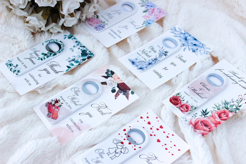 Pode incluir: Conjunto de seis abridores de garrafas de casamento com diferentes designs florais. Cada abridor tem um fundo branco com um design floral e o texto "Obrigado" e os nomes do casal e a data do casamento. Os designs incluem uma rosa vermelha, uma hort&ecirc;nsia azul, um design de folhas verdes, um carro vermelho, um design de cora&ccedil;&atilde;o branco e um design de casal branco.
