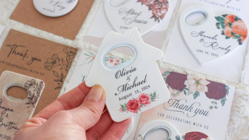 Pode incluir: Abridor de garrafas de cer&acirc;mica branca em forma de casa com um design floral e o texto "Olivia & Michael August 15, 2024".