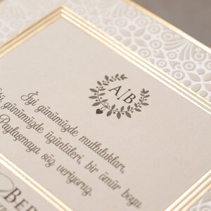 May include: A wedding invitation with a gold border and a floral design. The invitation features the initials "A/B" in a wreath and the text "İyi g&uuml;n&uuml;m&uuml;zde mutlulukları, &uuml;z&uuml;nt&uuml;leri, bir &ouml;m&uuml;r boyu paylaşmaya s&ouml;z veriyoruz. BERKAY".