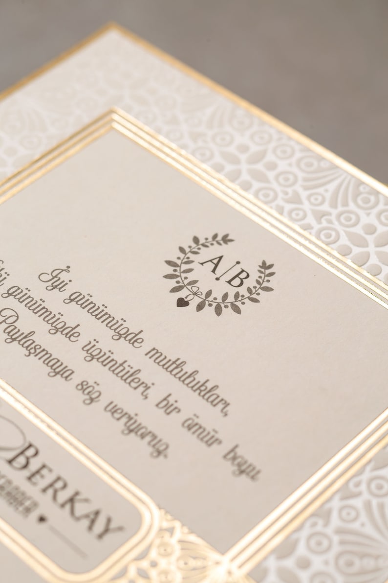 May include: A wedding invitation with a gold border and a floral design. The invitation features the initials "A/B" in a wreath and the text "İyi g&uuml;n&uuml;m&uuml;zde mutlulukları, &uuml;z&uuml;nt&uuml;leri, bir &ouml;m&uuml;r boyu paylaşmaya s&ouml;z veriyoruz. BERKAY".