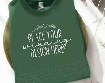 May include: A green sweatshirt mockup with the text "PLACE YOUR winning DESIGN HERE" in white. The sweatshirt is folded and lying on a wooden surface.