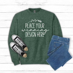 May include: A dark green sweatshirt with the text "Place your winning design here" in white. The sweatshirt is laid flat on a white wood background with a pair of black canvas shoes and blue jeans.