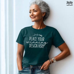 May include: A woman wearing a teal blue t-shirt with the text "Place your winning design here" on the front. She is standing in front of a white wall.