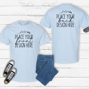 May include: A light blue t-shirt mockup with the text "PLACE YOUR FRONT DESIGN HERE" on the front and "PLACE YOUR BACK DESIGN HERE" on the back. The mockup includes a pair of black sneakers, blue jeans, and sunglasses.